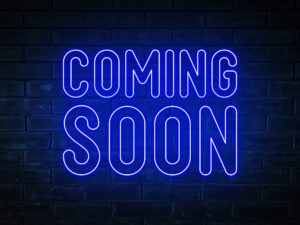 Coming soon - blue neon light word on brick wall background